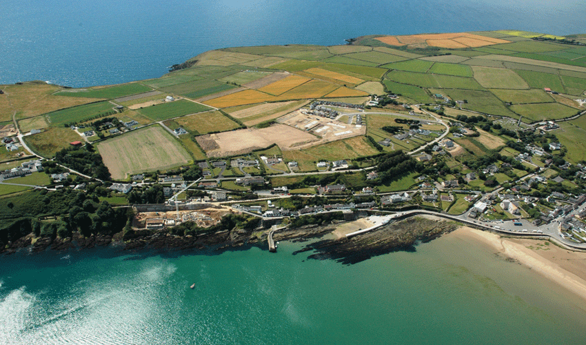 Aerial view of a coastal area with fields, buildings, and a body of water.