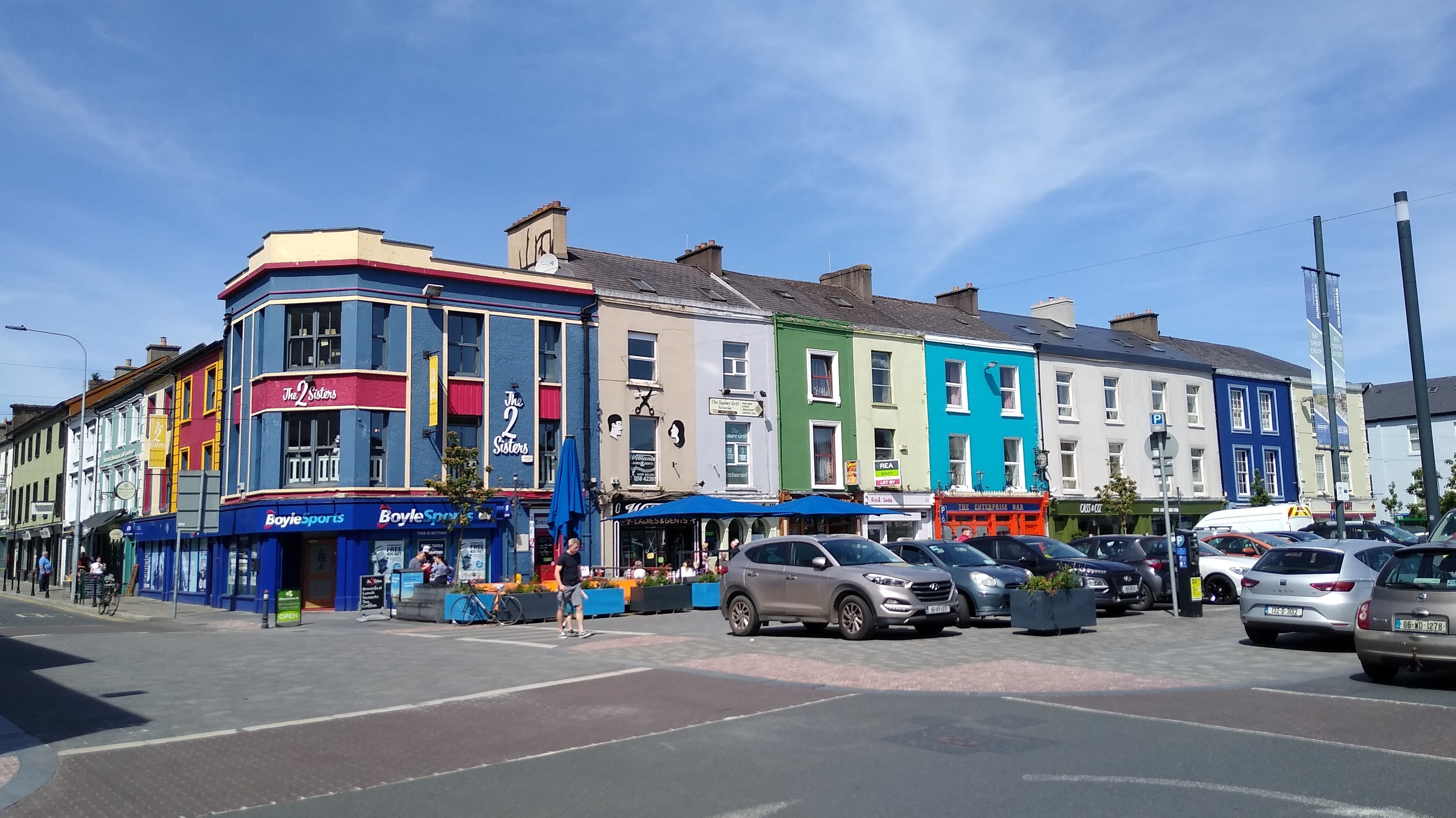 Colorful buildings on a street corner with cars and pedestrians in a town setting.