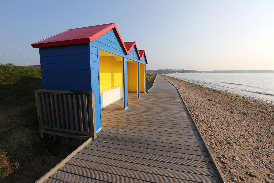 Colorful beach huts on a wooden boardwalk leading to a sandy beach.