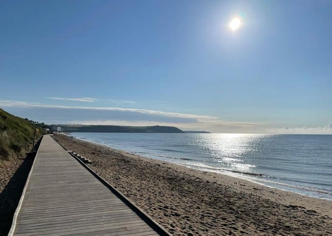 Beach scene with a wooden boardwalk leading to the ocean under a clear blue sky.